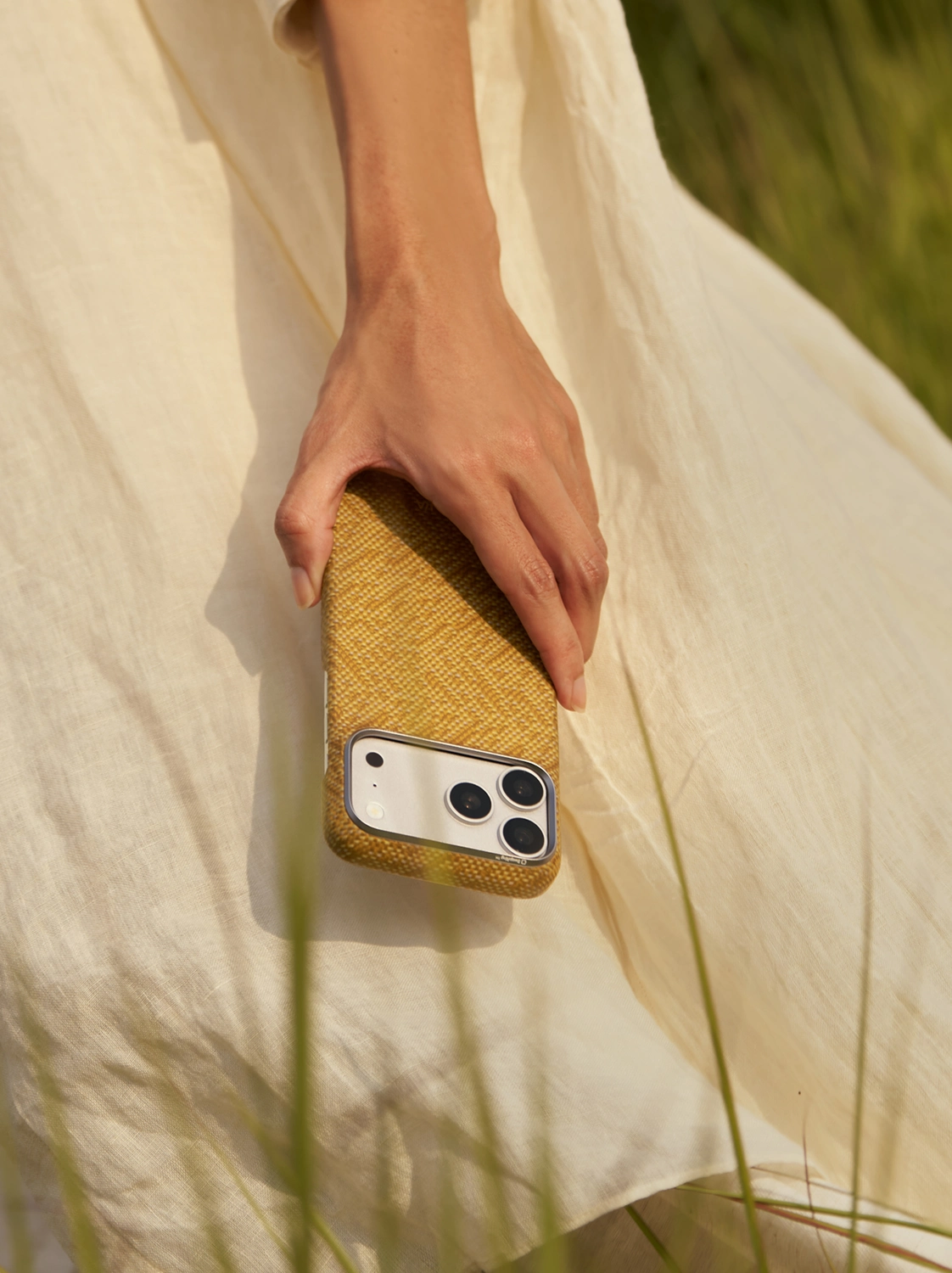 Golden Wind Over Wheat case held over a sunlit white dress